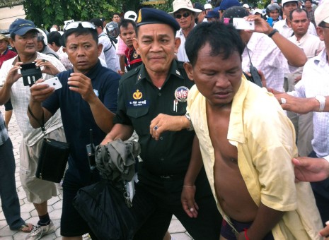 Poeurng Choeurn, who was discovered carrying a concealed pistol while taking pictures of monks at a rally in Phnom Penh's Freedom Park on Sunday, is escorted by military police after being set upon by rally participants who believed he planned to harm speakers at the meeting, which was attended by senior opposition CNRP members. (Kevin Doyle/The Cambodia Daily)
