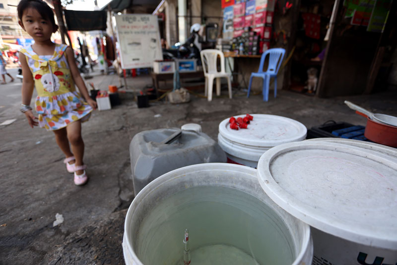 A child walks past buckets of acid for sale on Street 144 in Phnom Penh on Thursday. (Siv Channa)