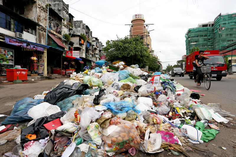 A cyclist covers his face as he passes a large pile of garbage on Sothearos Boulevard on Wednesday. (Siv Channa/The Cambodia Daily)