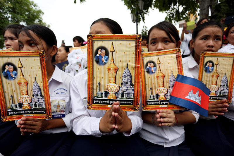 Young mourners hold up pictures of the ornate urn containing the late King Father’s ashes. (Siv Channa/The Cambodia Daily)