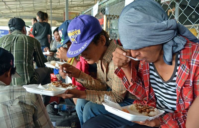 Migrant workers who were prevented from sneaking into Thailand eat food provided by the International Organization for Migration in Poipet City on Saturday. (Alex Consiglio/The Cambodia Daily)