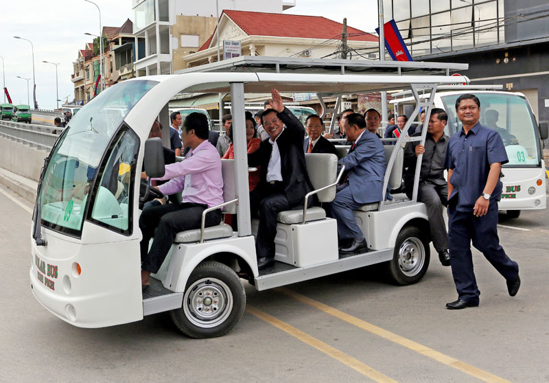 Prime Minister Hun Sen, seated next to his wife, Bun Rany, waves at reporters from a solar-powered buggy at the inauguration of the Stung Meanchey overpass in Phnom Penh on Thursday. Seated behind Mr. Hun Sen are Deputy Prime Minister Keat Chhon, left, and Phnom Penh Municipal Governor Pa Socheatvong. (Siv Channa/The Cambodia Daily)