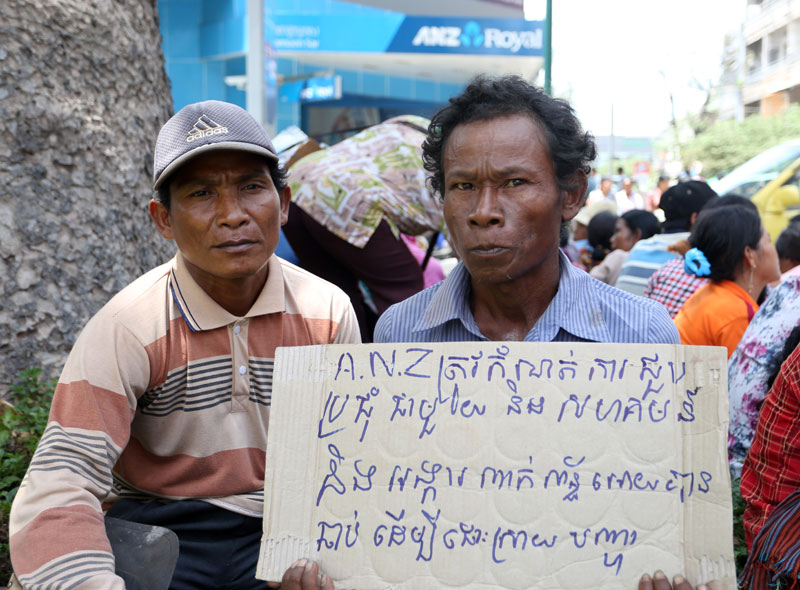 A villager holds up a sign reading 'ANZ must schedule a meeting immediately with the community and involved NGOs to find a solution' during a protest outside ANZ Royal's Phnom Penh headquarters on Thursday. (Siv Channa/The Cambodia Daily)