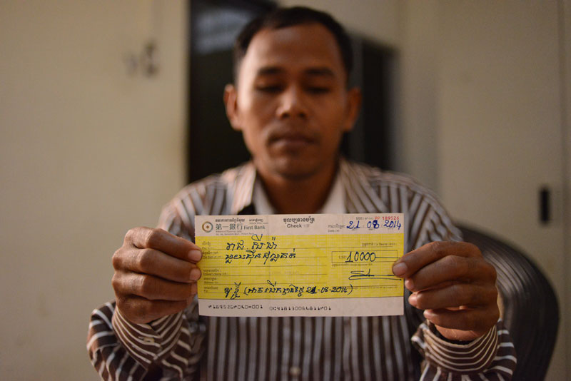 Reach Seima poses Tuesday with a bounced check he says was given to him by CPP lawmaker Lork Kheng. (Lauren Crothers/The Cambodia Daily)