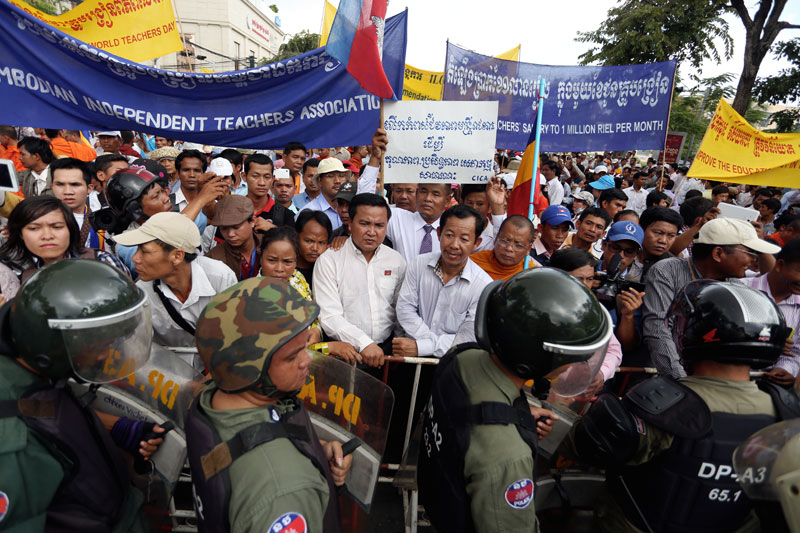 Rong Chhun, president of the Cambodian Independent Teachers' Association, center right, stands behind a barricade manned by riot police on Norodom Boulevard in Phnom Penh on Sunday during a protest to mark World Teachers' Day. (Siv Channa/The Cambodia Daily)