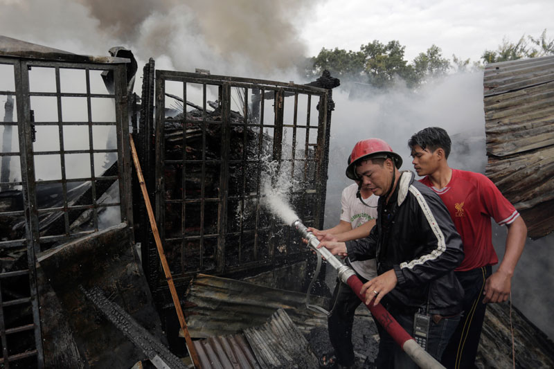 Vendors help a firefighter battle a blaze at Phnom Penh's Phsar Chas on Monday morning. (Siv Channa/The Cambodia Daily)