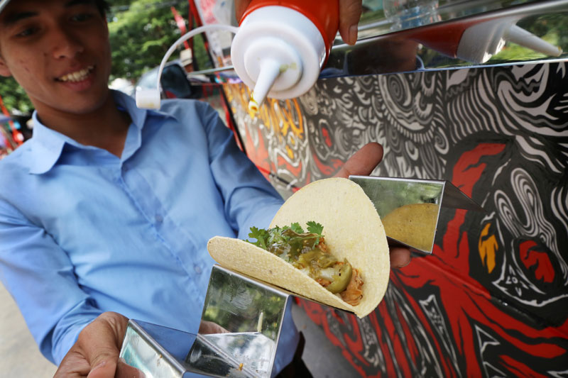 A man holds a taco on a platter as an Anabella's Hot Tacos vendor puts on green chili sauce. (Aria Danaparamita/The Cambodia Daily)