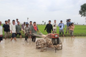 Prime Minister Hun Sen, flanked by ministers, bodyguards and government officials, steers a motorized plow in a rice paddy in Kandal province in 2013. (Sok Chamroeun)