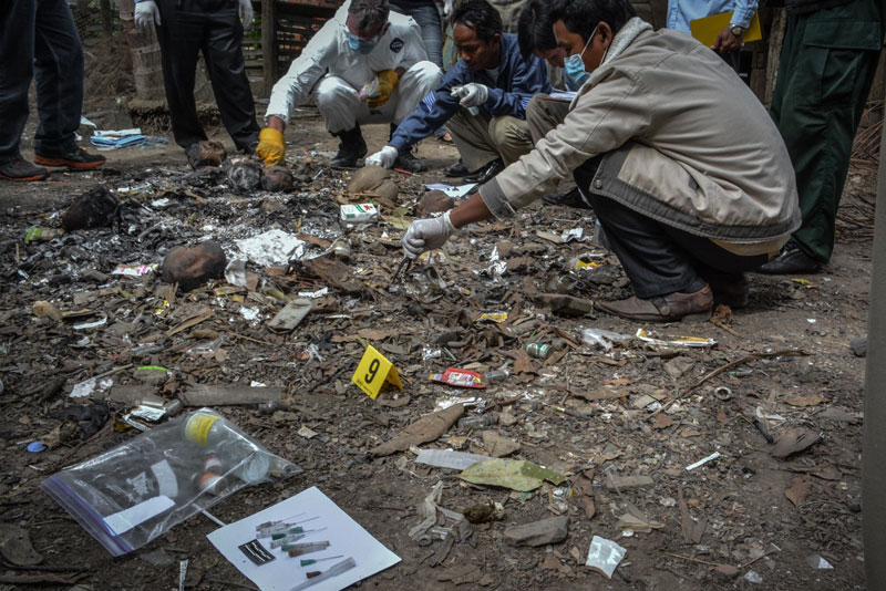 Police and other investigators collect medical equipment from the remnants of a trash fire in the yard outside the home of Yem Chrin last week. (Alex Consiglio/The Cambodia Daily)