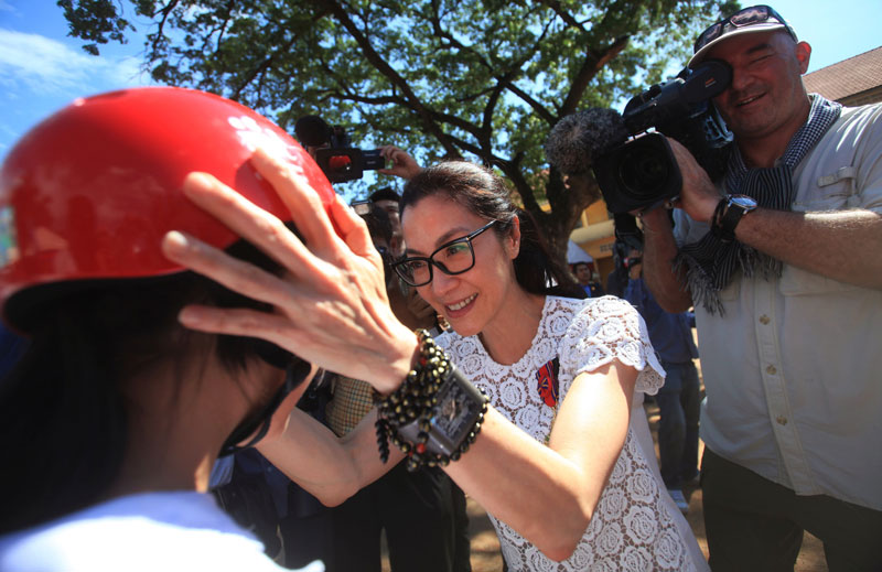 Actress Michelle Yeoh puts a motorbike helmet on a student at Phnom Penh's Tuol Svay Prey primary school on Tuesday. (Pring Samring/Reuters)