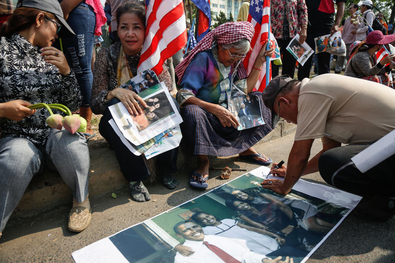 An activist writes on a poster bearing an image of U.S. President Barack Obama and his family during a protest outside the U.S. Embassy in Phnom Penh on Tuesday. (Siv Channa/The Cambodia Daily)