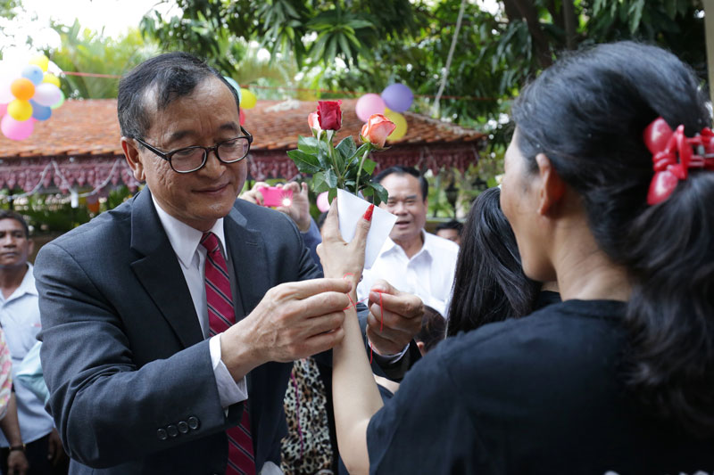 Opposition leader Sam Rainsy ties a red thread around the wrist of a freed land-rights activist at deputy opposition leader Kem Sokha's house in Phnom Penh on Saturday. (Satoshi Takahashi)