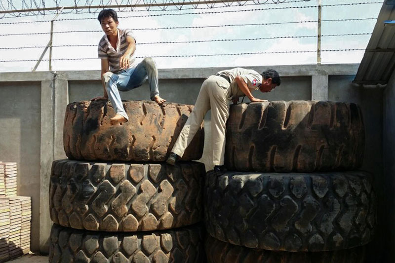 A police officer looks into a stack of tires at a furniture shop in Phnom Penh on Thursday as a Vietnamese migrant worker jumps down from another stack after being found inside. (Uk Heisela)