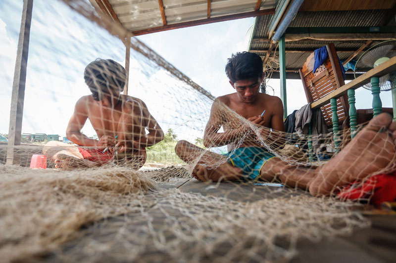 Wing Ling, right, and his brother repair fishing nets on the porch of their floating home on the Mekong River on Wednesday. (Siv Channa/The Cambodia Daily)