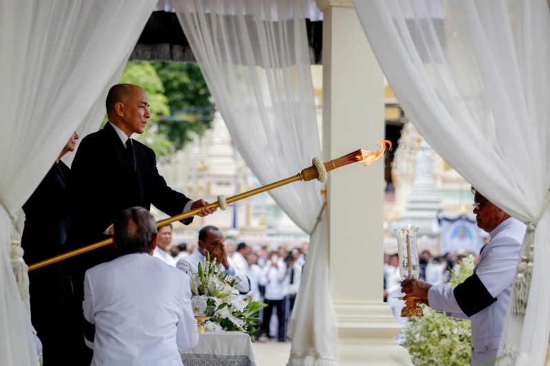King Norodom Sihamoni lights a scepter from a candle held out by Interior Minister Sar Kheng ahead of the late CPP president's cremation on Friday. (Siv Channa/The Cambodia Daily)