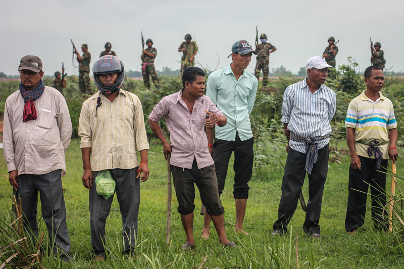 A row of Cambodian men armed with wooden clubs stand in front of Cambodian soldiers about a kilometer from the Vietnamese border in Svay Rieng province, where they confronted hundreds of activists who were led to the area by a group of opposition lawmakers last year. (Alex Willemyns/The Cambodia Daily)