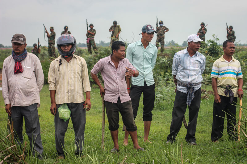 A row of Cambodian men armed with wooden clubs stand in front of Cambodian soldiers about a kilometer from the Vietnamese border in Svay Rieng province, where they confronted hundreds of activists who were led to the area by a group of opposition lawmakers Sunday. (Alex Willemyns/The Cambodia Daily)