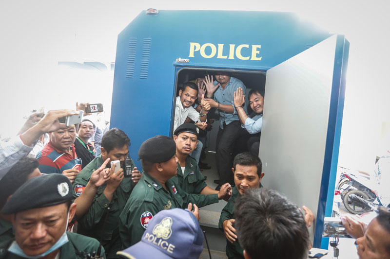 Meach Sovannara, chief of the CNRP's information department, left, and Oeur Narith, right, an assistant to opposition lawmaker Mu Sochua, wave from a police truck at the Phnom Penh Municipal Court on Tuesday after being sentenced to 20 years in prison for leading an insurrection. (Siv Channa/The Cambodia Daily)