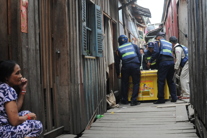 A woman sits outside her home Friday in Phnom Penh's Trapaing Chhouk village as police remove a gaming machine from a shack. (Simon Henderson/The Cambodia Daily)
