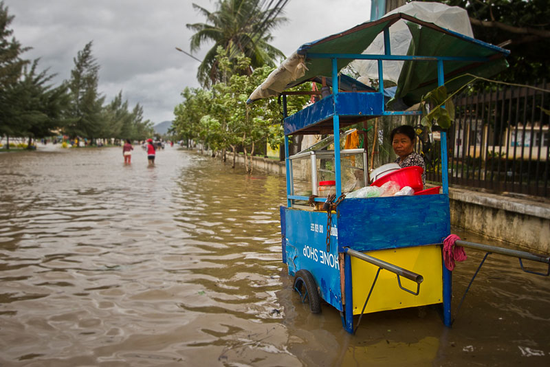 A vendor stands behind her cart on a flooded street in Kampot City on Thursday. (Nicolas Malinowski)