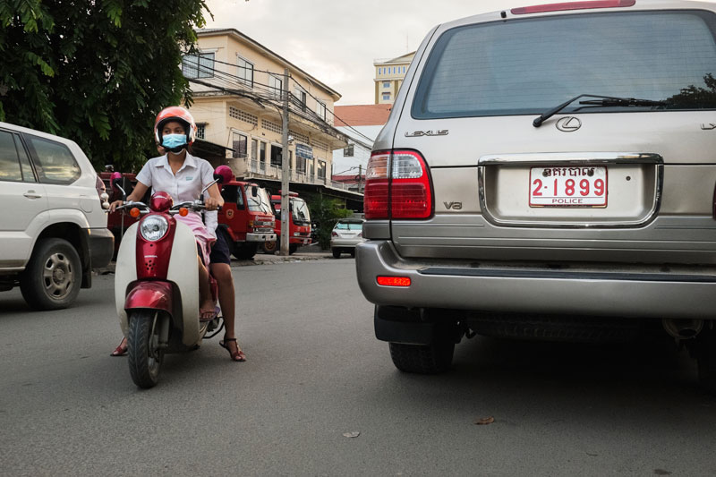 A girl drives past a Lexus SUV with a police license plate in Phnom Penh on Wednesday. (Jens Welding Ollgaard/The Cambodia Daily)
