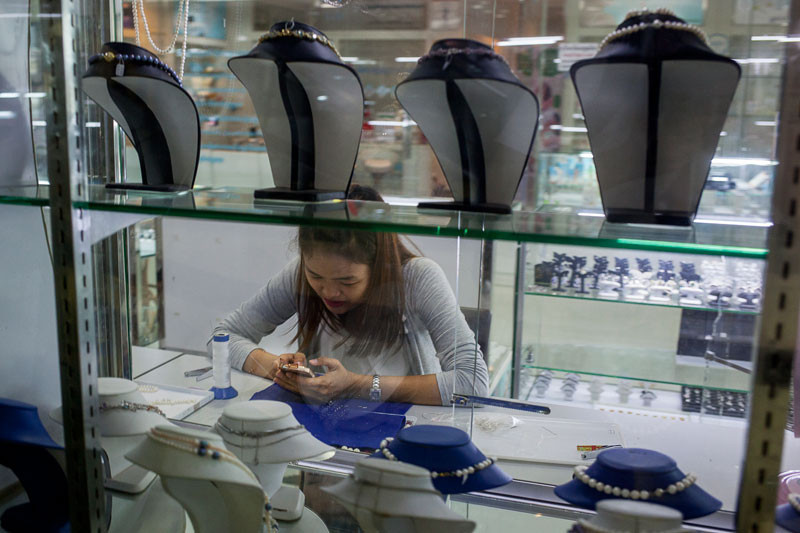 A women looks at her smartphone behind a jewelry display at a shop Penh’s Paragon mall this week. (Jens Welding Ollgaard/The Cambodia Daily)