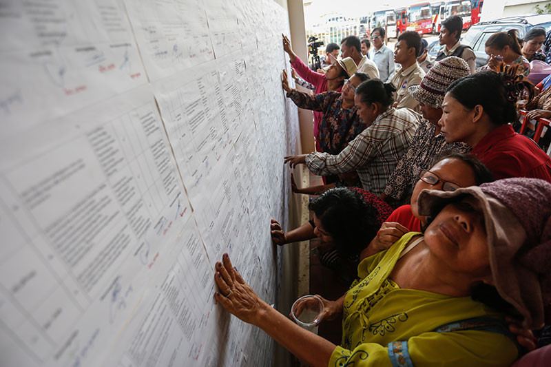 Borei Keila residents search for their names on sheets of paper listing compensation packages at the Prampi Makara district office in Phnom Penh on Friday. (Siv Channa/The Cambodia Daily)