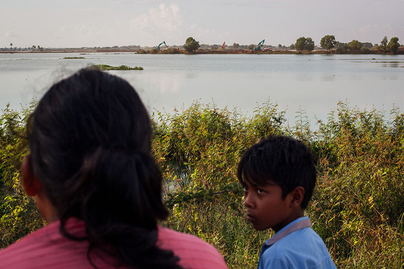 Nuo Nim, left, looks out on Wednesday at the lake and excavation site that merged after a sliver of land separating them collapsed on Tuesday night. (Jens Welding Ollgaard/The Cambodia Daily)