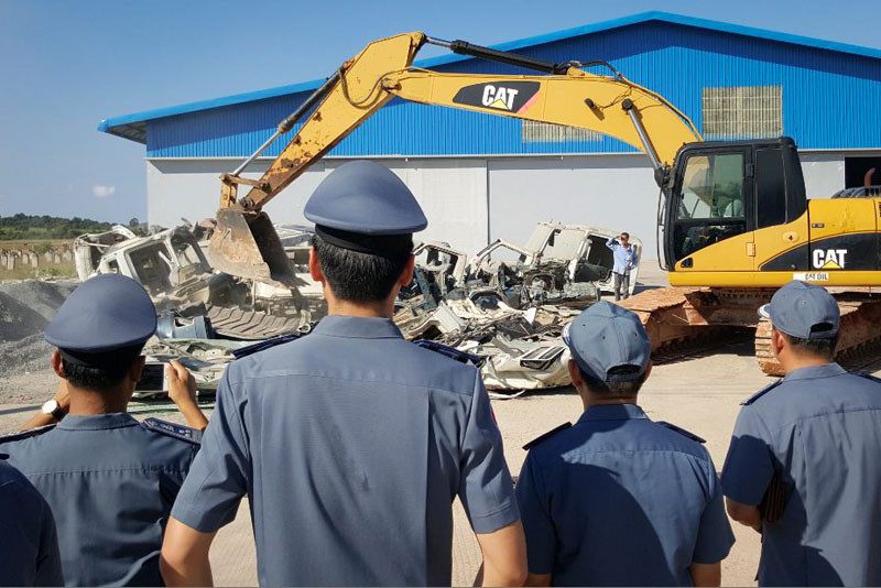 Officials watch an excavator destroy truck cabs that were deemed unfit for the road, at the Stung Hav Special Economic Zone and Port in Preah Sihanouk province on Wednesday. (Den Seymar)