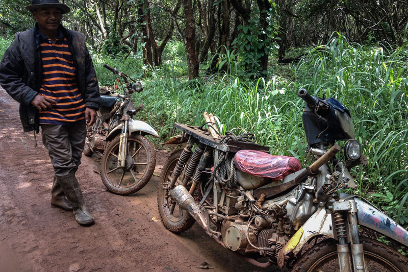A timber scavenger stands next to his customized motorbike, used to lug up to 500 kg of wood, on a dirt track inside the Veasna Investment concession in Ratanakkiri in September. (Matt Blomberg/The Cambodia Daily)