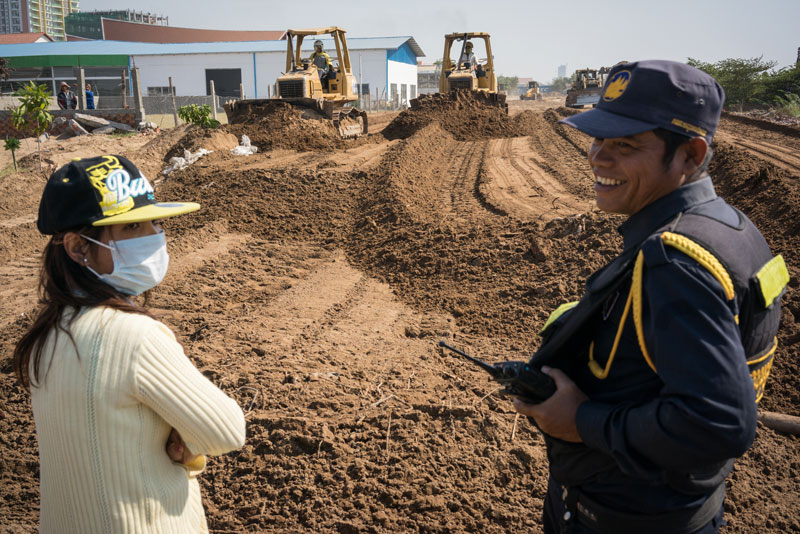 A security guard speaks with a local woman as bulldozers flatten a strip of land in Phnom Penh's Chroy Changva district on Monday. (Ben Woods/The Cambodia Daily)