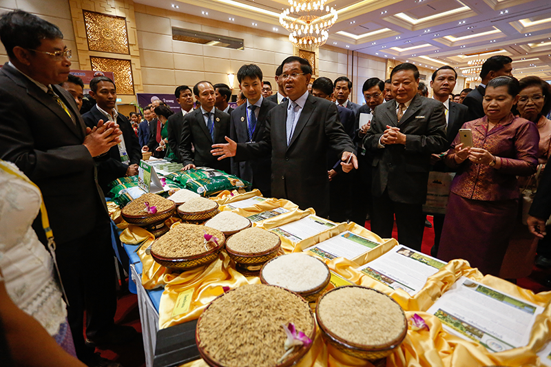 Prime Minister Hun Sen speaks to exhibitors next to Cambodia Rice Federation president Sok Puthyvuth (center) at the Cambodia Rice Forum on Monday. In a speech at the forum, Mr. Hun Sen said that the country’s rice sector had suffered due in part to strong competition from regional neighbors, and said that increased investment was needed to boost exports. (Siv Channa/The Cambodia Daily)