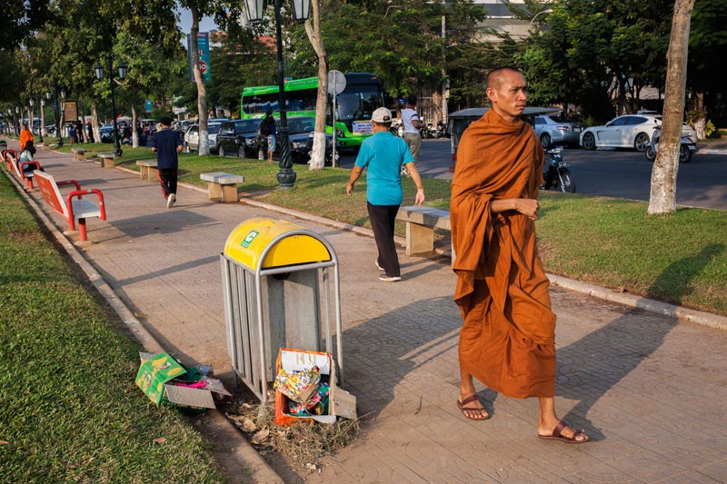 A monk walks past a trash can surrounded by garbage at Wat Botum Park in Phnom Penh on Tuesday. (Jens Welding Ollgaard/The Cambodia Daily) 