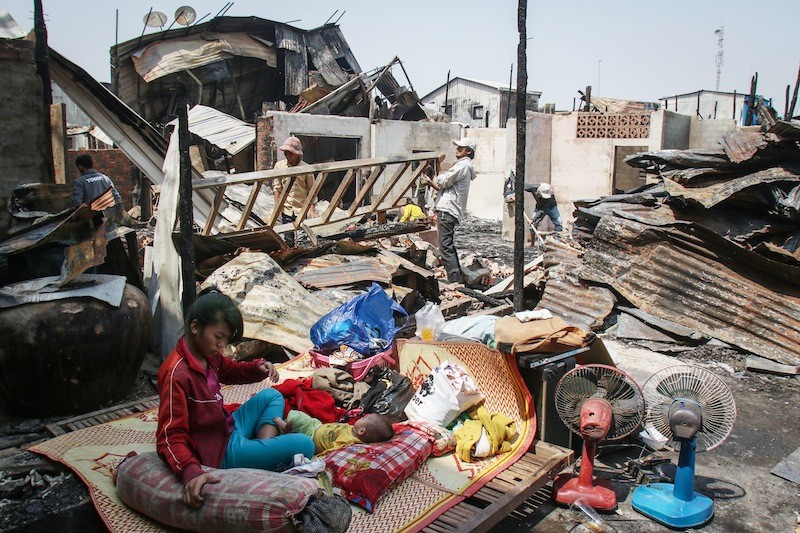 A girl and baby sit on a mat as residents sift through the remains of their homes after a fire destroyed 97 houses in Phnom Penh’s Meanchey district yesterday morning. (Khem Sovannara)