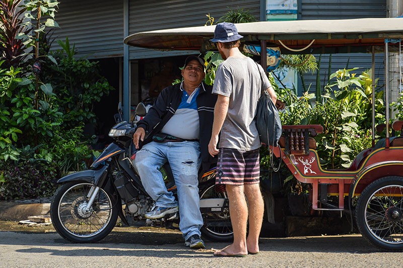 Tuk-tuk driver Nin Sakovey speaks with a customer outside the Tuol Sleng Genocide Museum in Phnom Penh in April. (Ben Paviour/The Cambodia Daily)