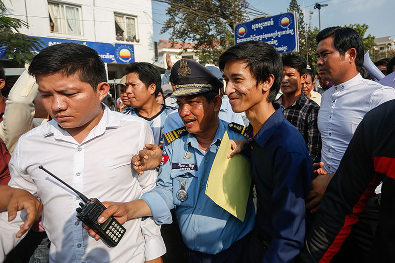 A police officer escorts Srey Chamroeun through a crowd of protesters and opposition supporters outside the CNRP’s headquarters in Phnom Penh on Friday. (Siv Channa/The Cambodia Daily)