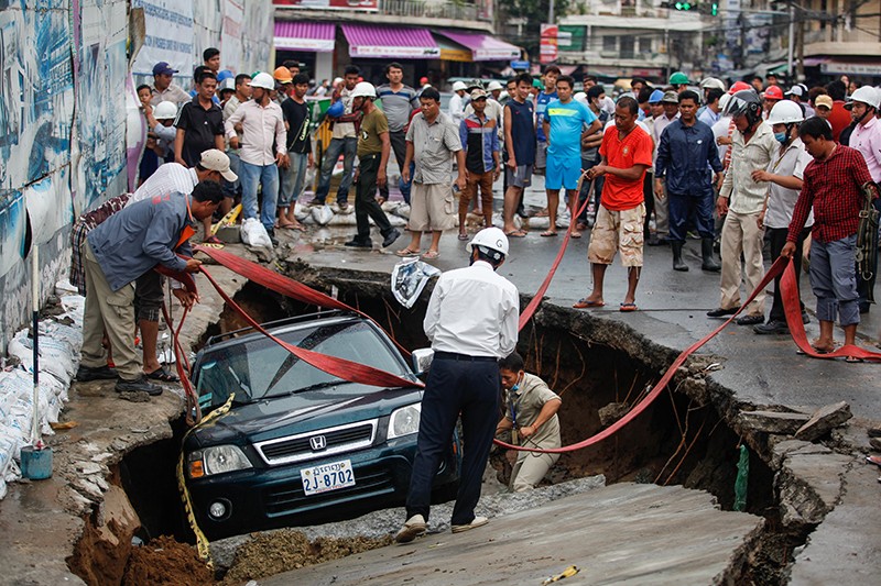 Men prepare to lift a car—with the help of a crane—out of a sinkhole on Wednesday after a section of road collapsed during a rainstorm in Phnom Penh. (Siv Channa/The Cambodia Daily) 