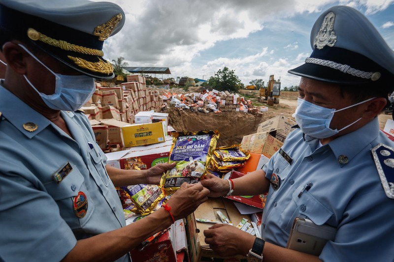 Police officials examine packages of Vietnamese coffee, one of many items burned at Choeung Ek landfill in Phnom Penh yesterday as part of an effort to warn Cambodians of the health risks of consuming expired and counterfeit products. (Siv Channa/The Cambodia Daily)
