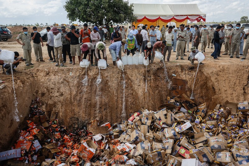 Workers douse expired and counterfeit Vietnamese products with fuel on Thursday at the Choeung Ek landfill in Phnom Penh. (Siv Channa/The Cambodia Daily)