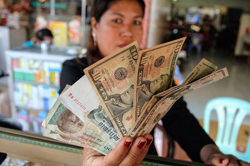 A woman working at a money exchange kiosk in Phnom Penh holds up US dollars and Cambodian riel in January 2011. (Pring Samrang/Reuters)
