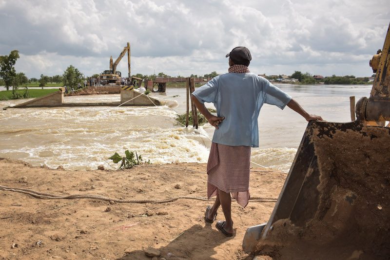A local resident watches flood water rush over the collapsed Sandor Dam in Phnom Penh’s Dangkao district on Tuesday. (Rayna Stackhouse/The Cambodia Daily)