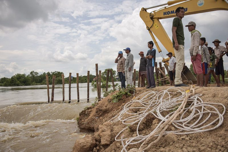 Local residents and officials look watch flood water rushes over the collapsed Sandor Dam in Phnom Penh’s Dangkao district on Tuesday. (Rayna Stackhouse/The Cambodia Daily)