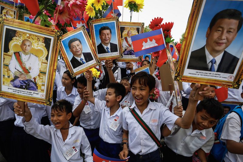 Students holding up images of Chinese President Xi Jinping and King Norodom Sihamoni stand along Sothearos Boulevard awaiting Mr. Xi’s arrival in Phnom Penh on Thursday. (Siv Channa/The Cambodia Daily)