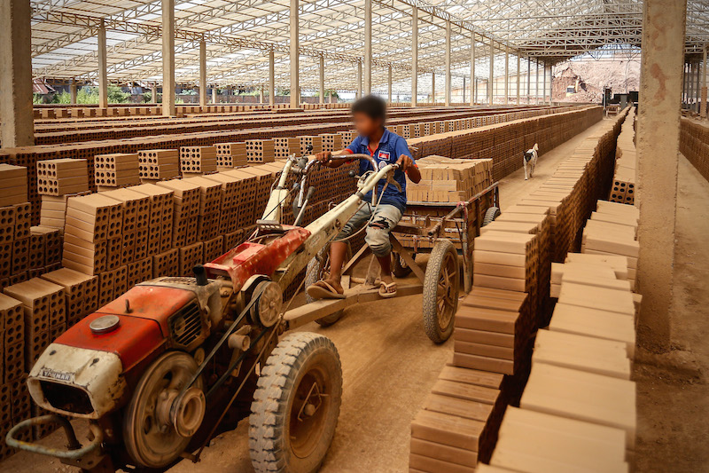 A 14-year-old boy drives away a pile of bricks at a factory in Kandal province last week. (Siv Channa/The Cambodia Daily)